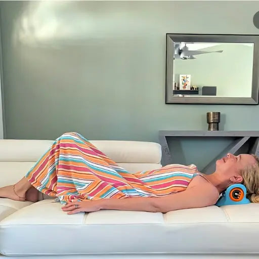 Person lying on a couch with a colorful striped garment, wearing an orange neck pillow.